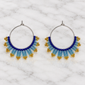 Pair of handmade beaded hoop earrings with royal blue, icy blue and gold seed beads on white marble