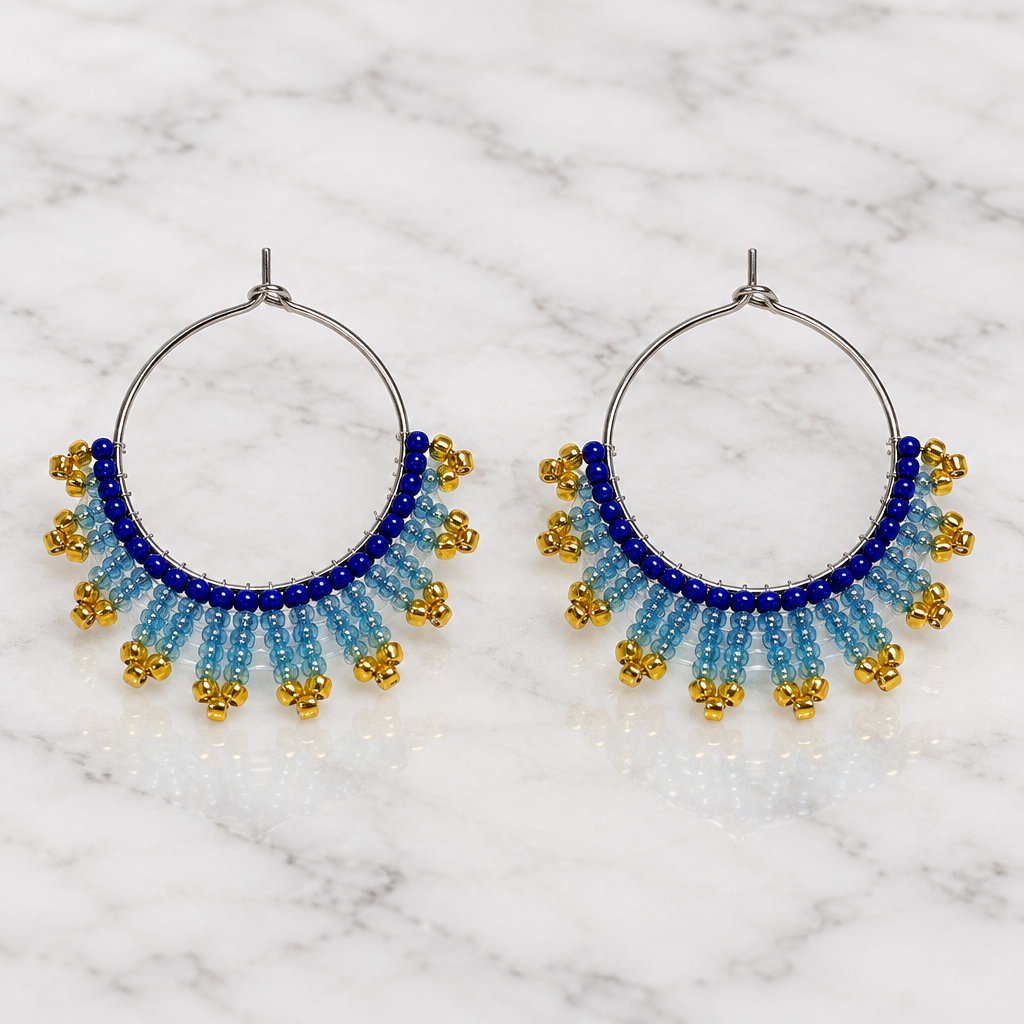 Pair of handmade beaded hoop earrings with royal blue, icy blue and gold seed beads on white marble