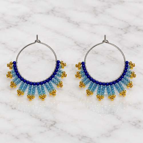 Pair of handmade beaded hoop earrings with royal blue, icy blue and gold seed beads on white marble