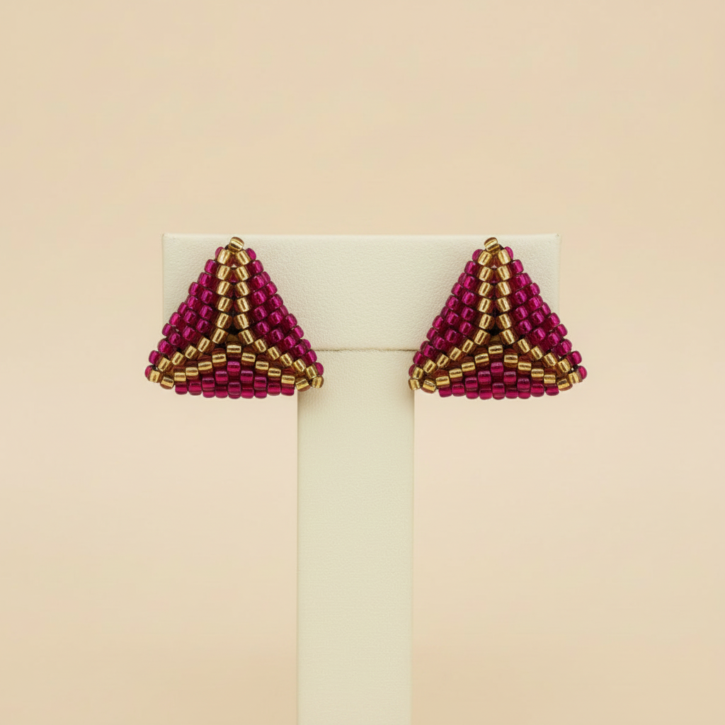 Matching pair of pink-and-gold beaded earrings on an ivory stand